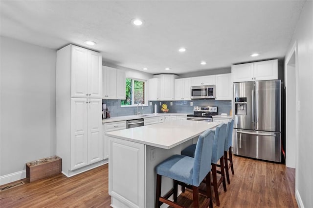 215 E Edgewood Dr, Peters Twp, PA 15317 - kitchen with appliances with stainless steel finishes, wood finished floors, tasteful backsplash, a breakfast bar area, and white cabinetry