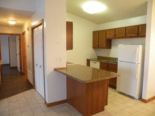 kitchen featuring white appliances, kitchen peninsula, and light tile floors