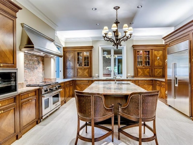 kitchen with an island with sink, high end appliances, light stone countertops, an inviting chandelier, and decorative light fixtures