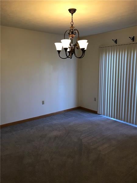 unfurnished room featuring a chandelier and dark carpet