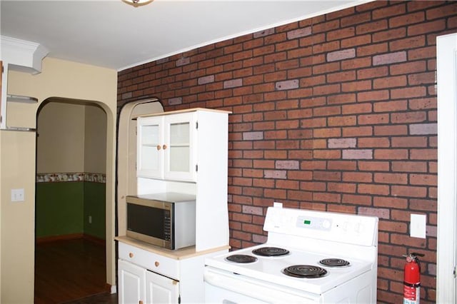 kitchen with brick wall, dark hardwood / wood-style floors, range, and white cabinetry