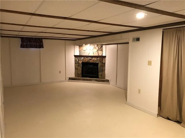 basement featuring a paneled ceiling and a stone fireplace