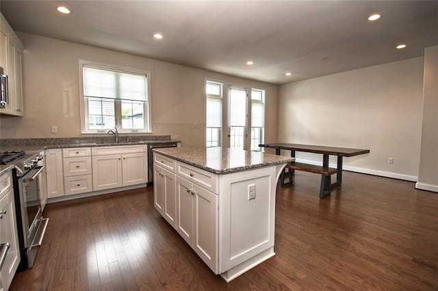 kitchen with dark wood-type flooring, white cabinets, a center island, stone countertops, and stainless steel stove