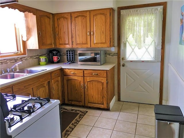 kitchen with light tile floors, range, tasteful backsplash, and sink