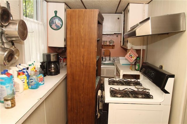 kitchen featuring wall chimney exhaust hood, a drop ceiling, white gas stove, and white cabinets