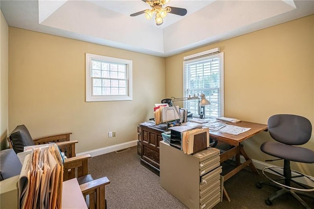 carpeted office featuring ceiling fan, plenty of natural light, and a raised ceiling