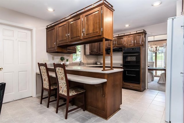 kitchen with white fridge, a kitchen breakfast bar, double oven, kitchen peninsula, and a chandelier