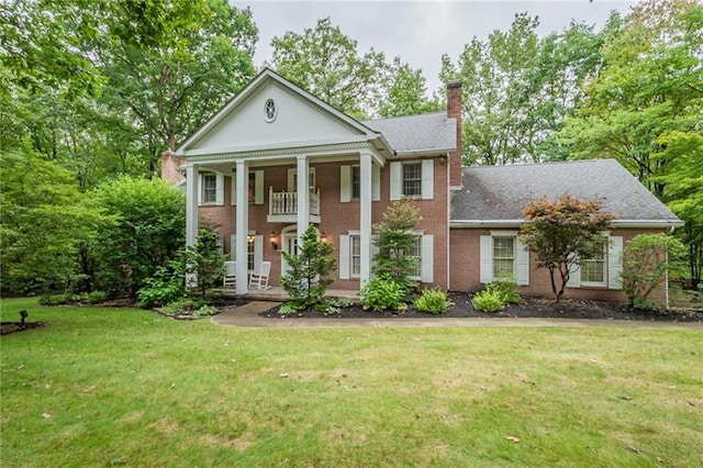 greek revival inspired property with a front lawn and a balcony