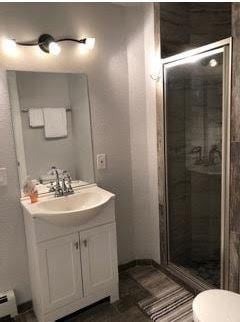 bathroom with a baseboard radiator, toilet, large vanity, and walk in shower