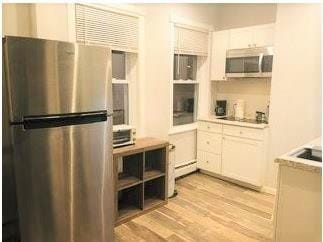 kitchen with white cabinets, a baseboard heating unit, light hardwood / wood-style flooring, and stainless steel appliances