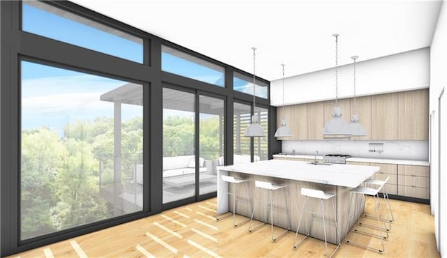 kitchen with an island with sink, light hardwood / wood-style floors, decorative light fixtures, light brown cabinetry, and a breakfast bar area