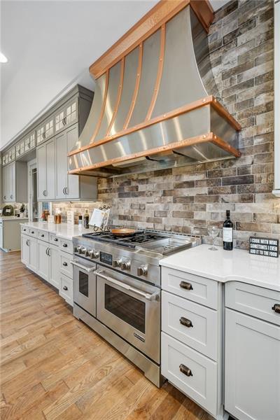 kitchen with backsplash, premium range hood, range with two ovens, and light hardwood / wood-style floors