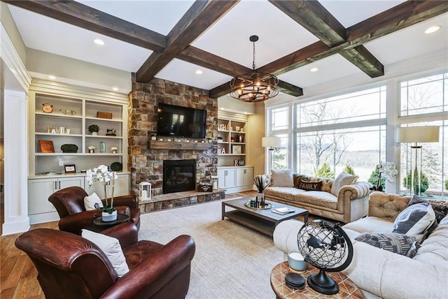 living room with a chandelier, light hardwood / wood-style floors, a stone fireplace, and beamed ceiling