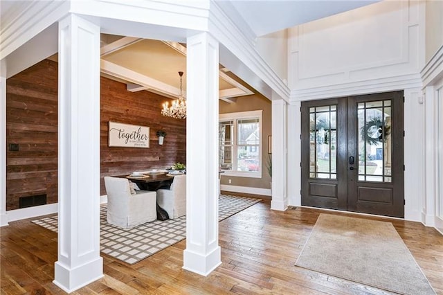 entrance foyer with wood walls, ornate columns, a chandelier, light hardwood / wood-style floors, and french doors