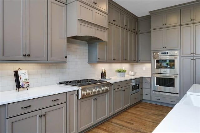 kitchen with gray cabinets, tasteful backsplash, stainless steel appliances, and light wood-type flooring