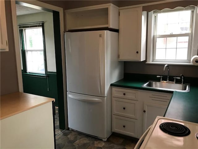 kitchen featuring white cabinetry, white fridge, sink, stove, and dark tile flooring