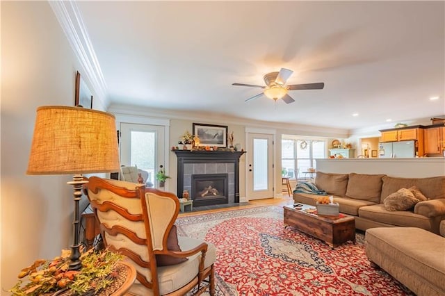 living room with a tiled fireplace, ceiling fan, and crown molding