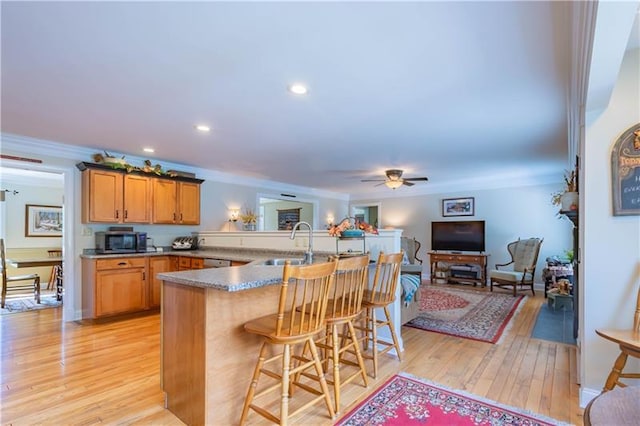 kitchen featuring crown molding, a kitchen bar, light hardwood / wood-style flooring, ceiling fan, and sink