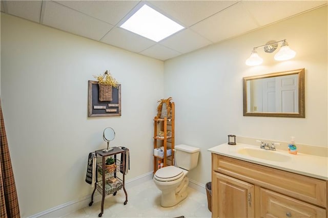 bathroom with tile flooring, toilet, a paneled ceiling, and vanity