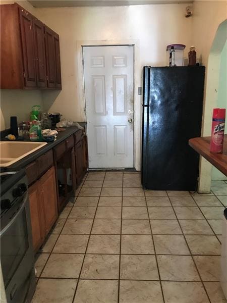 kitchen featuring stainless steel electric range, black fridge, sink, and light tile floors