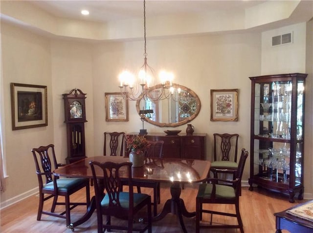 dining space featuring a notable chandelier, light hardwood / wood-style floors, and a raised ceiling