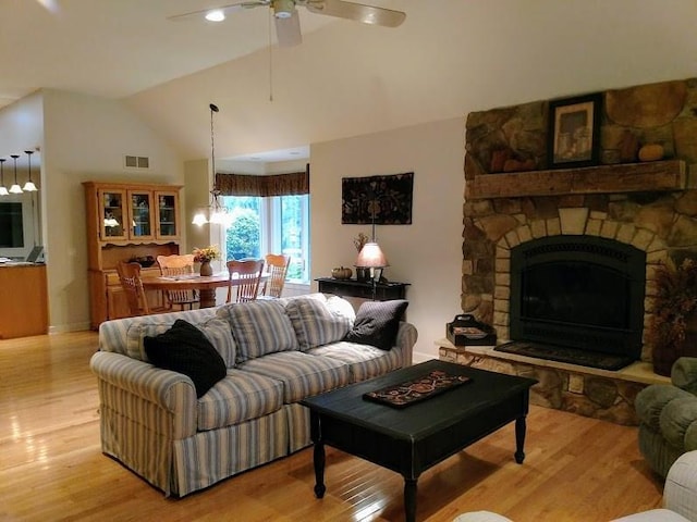 living room featuring a fireplace, lofted ceiling, ceiling fan with notable chandelier, and light wood-type flooring