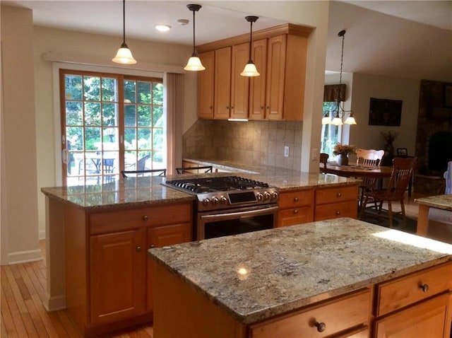 kitchen featuring a kitchen island, decorative light fixtures, stainless steel stove, backsplash, and light wood-type flooring