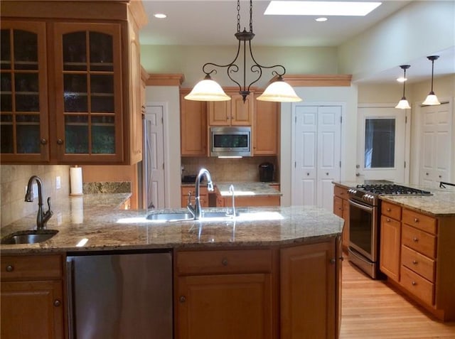 kitchen with pendant lighting, sink, stainless steel appliances, tasteful backsplash, and light wood-type flooring