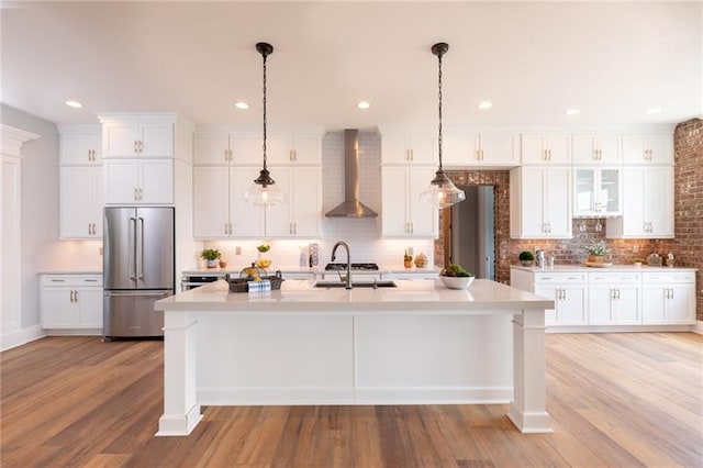 kitchen featuring light hardwood / wood-style floors, hanging light fixtures, high end fridge, and wall chimney range hood