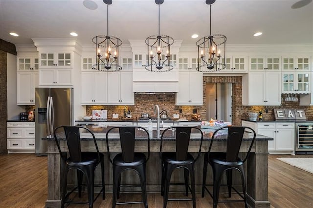 kitchen featuring hanging light fixtures, stainless steel fridge, a kitchen island with sink, a kitchen breakfast bar, and a chandelier