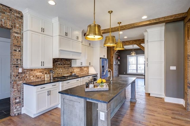 kitchen featuring white cabinets, a center island with sink, light wood-type flooring, pendant lighting, and a kitchen breakfast bar