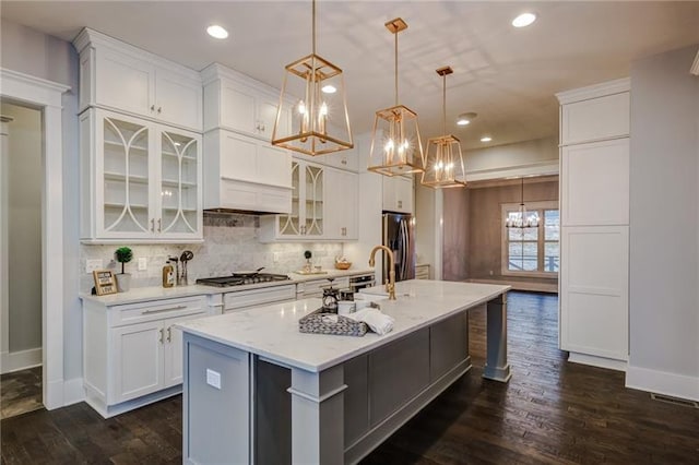 kitchen featuring white cabinets, a kitchen bar, dark hardwood / wood-style floors, an island with sink, and hanging light fixtures