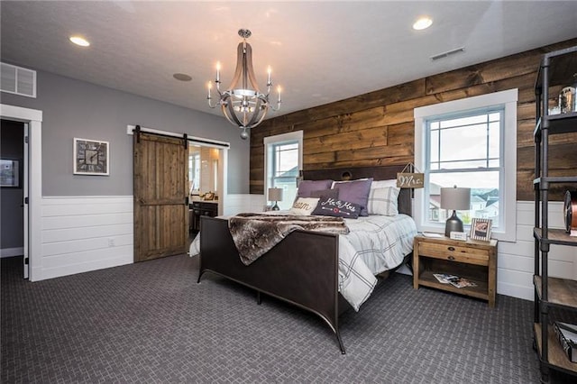 bedroom featuring a barn door, an inviting chandelier, and dark colored carpet