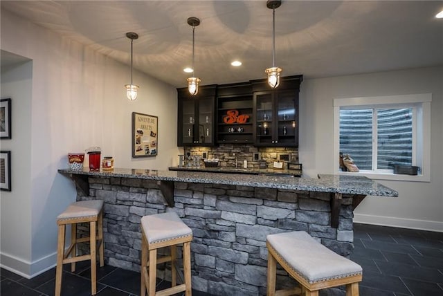 bar with light stone counters, dark tile flooring, tasteful backsplash, decorative light fixtures, and dark brown cabinetry