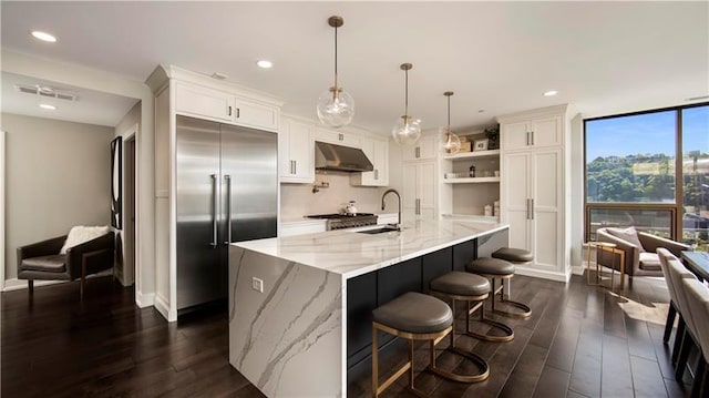 kitchen featuring pendant lighting, built in refrigerator, white cabinets, light stone counters, and dark hardwood / wood-style flooring