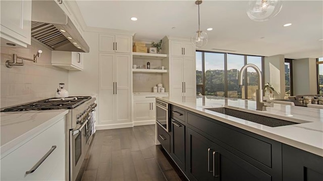 kitchen with hanging light fixtures, wall chimney range hood, tasteful backsplash, white cabinetry, and range with two ovens