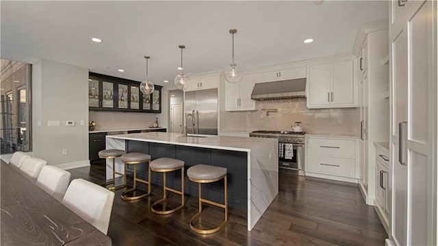 kitchen with hanging light fixtures, dark hardwood / wood-style flooring, premium appliances, a center island with sink, and white cabinetry