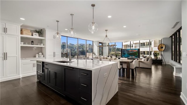 kitchen with sink, a center island with sink, dark wood-type flooring, decorative light fixtures, and white cabinetry