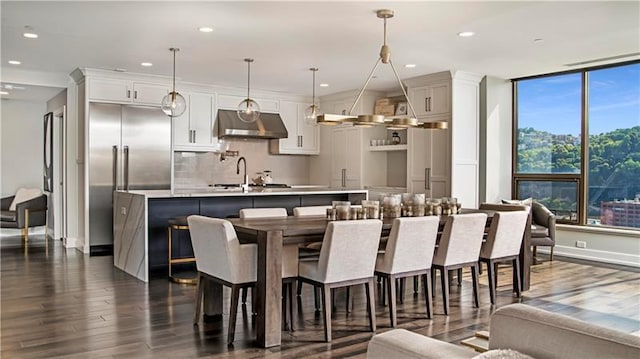 kitchen with a kitchen bar, dark wood-type flooring, hanging light fixtures, and a kitchen island with sink