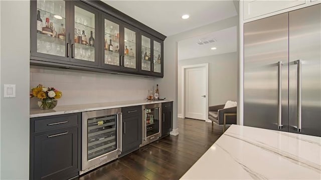 bar with wine cooler, built in fridge, dark hardwood / wood-style floors, and light stone counters