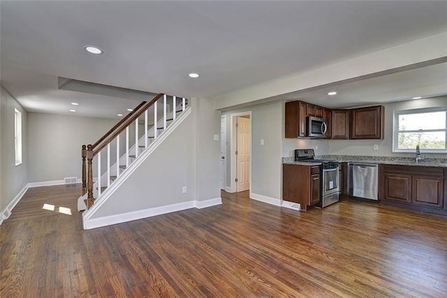 kitchen with dark brown cabinetry, dark hardwood / wood-style floors, stainless steel appliances, light stone countertops, and sink