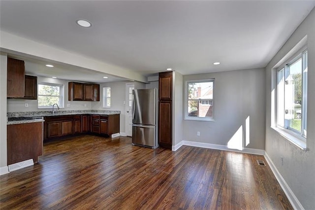 kitchen with stainless steel fridge, dark hardwood / wood-style flooring, sink, dark brown cabinets, and light stone countertops