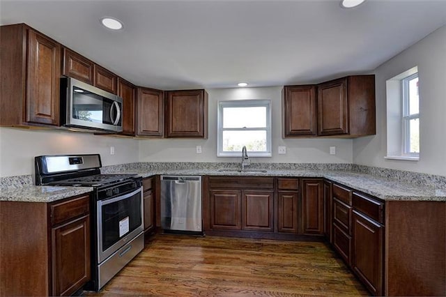 kitchen featuring stainless steel appliances, light stone countertops, dark wood-type flooring, dark brown cabinetry, and sink