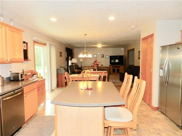 kitchen with light tile flooring, a kitchen island, stainless steel appliances, a notable chandelier, and light brown cabinets