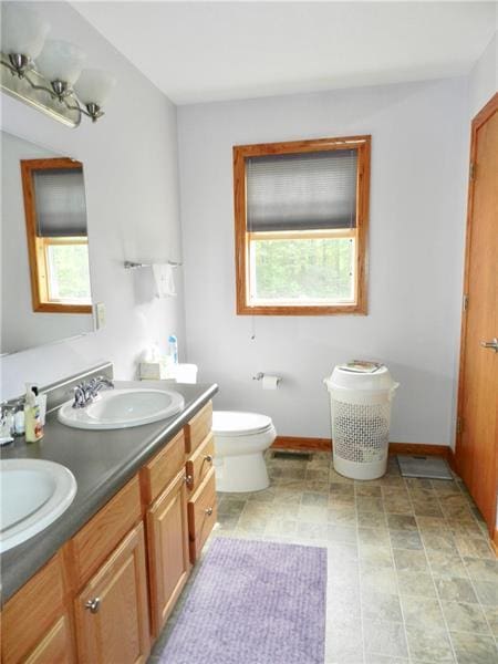 bathroom featuring tile flooring, dual bowl vanity, toilet, and a healthy amount of sunlight