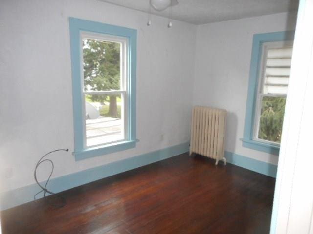 spare room featuring dark wood-type flooring and radiator