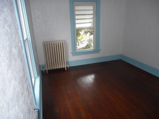 empty room with dark wood-type flooring and radiator