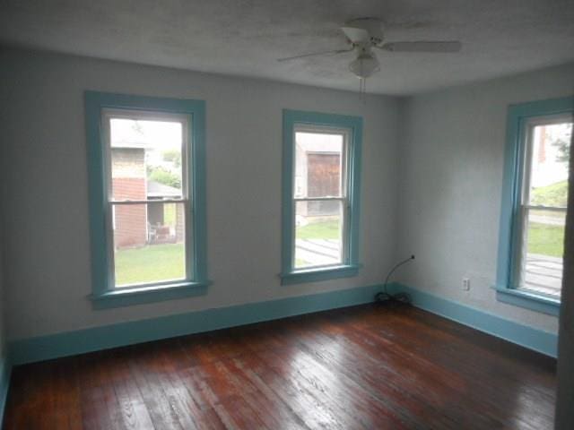 spare room featuring dark hardwood / wood-style floors, ceiling fan, and a healthy amount of sunlight