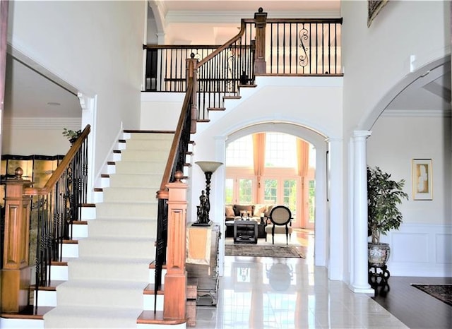 stairway featuring tile floors, ornamental molding, decorative columns, and a high ceiling