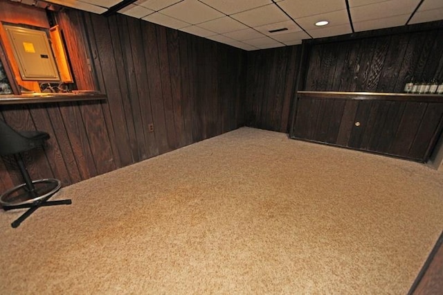 empty room with wooden walls, carpet flooring, and a drop ceiling